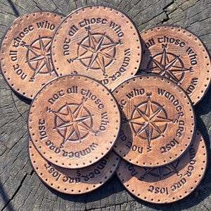 May include: Six brown leather coasters with a compass design and the text "Not all those who wander are lost".