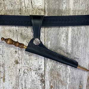 May include: A black leather sheath with a cross-shaped metal accent, attached to a black leather belt. A wooden stick is partially inserted into the sheath.