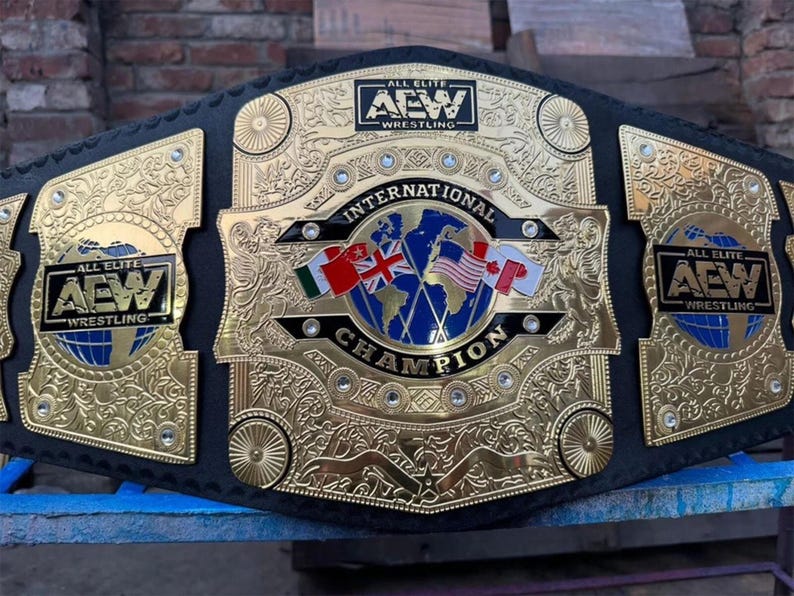 May include: A gold and black wrestling championship belt. The belt features the text "ALL ELITE AEW WRESTLING" on the side plates and "INTERNATIONAL CHAMPION" on the center plate. Flags of different countries are also displayed.