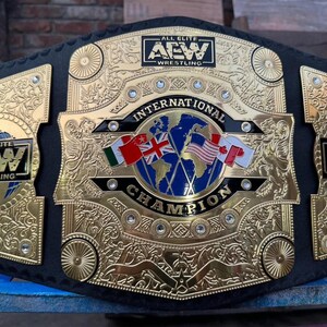 May include: A gold and black wrestling championship belt. The center plate features a globe with flags of Ireland, the United Kingdom, the United States, and Canada. The belt reads "INTERNATIONAL CHAMPION" and "ALL ELITE WRESTLING".