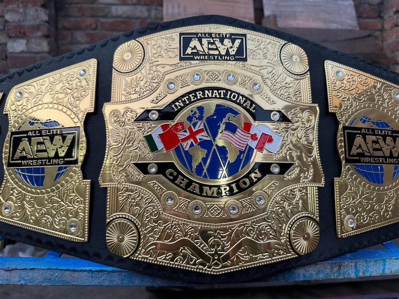 May include: A gold and black wrestling championship belt. The center plate features a globe with flags of Ireland, the United Kingdom, the United States, and Canada. The belt reads "INTERNATIONAL CHAMPION" and "ALL ELITE WRESTLING".