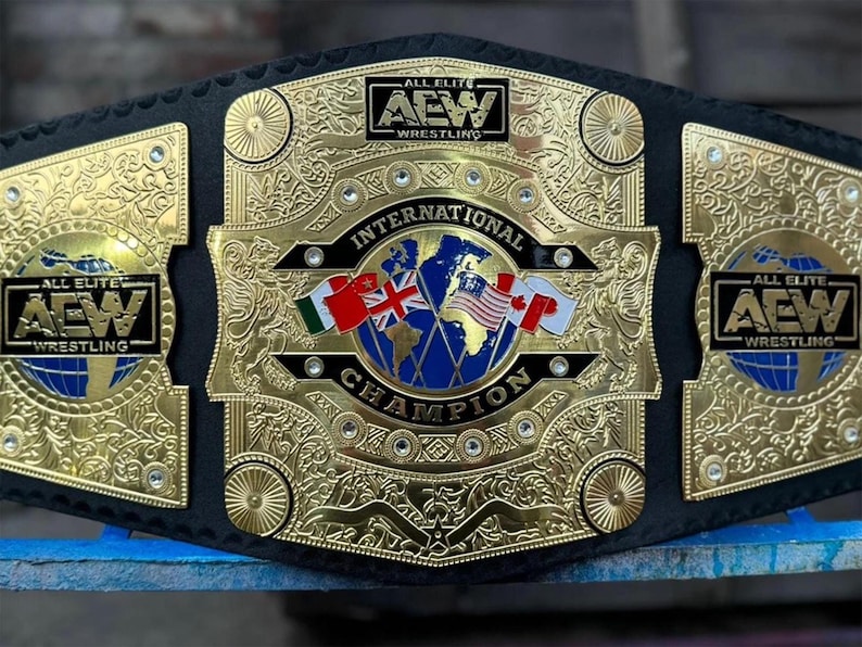 May include: A gold and black wrestling championship belt. The center plate reads "INTERNATIONAL CHAMPION" with a globe and flags. The belt has "ALL ELITE AEW WRESTLING" on the side plates.