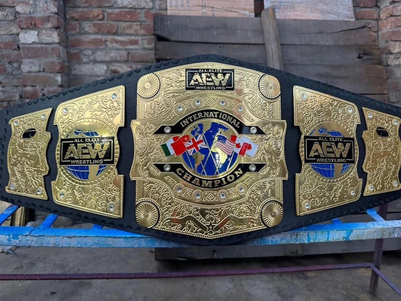 May include: A gold and black wrestling championship belt with the text "ALL ELITE WRESTLING" and "INTERNATIONAL CHAMPION". The belt features gold filigree and the flags of several countries.