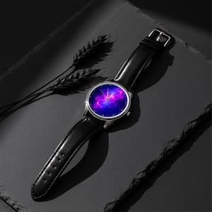 May include: A wristwatch with a black leather band and a silver-colored case. The watch face displays a vibrant galaxy design with shades of purple, pink, and blue. The watch is set against a dark background with a sprig of wheat.