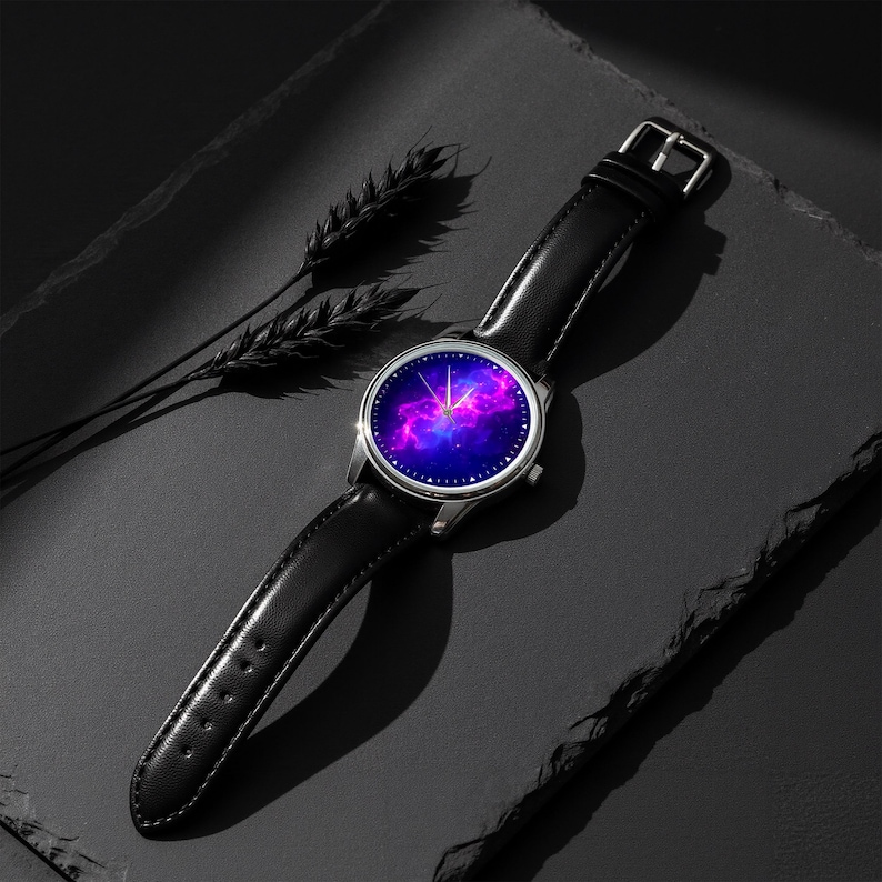 May include: A wristwatch with a black leather band and a silver-colored case. The watch face displays a vibrant galaxy design with shades of purple, pink, and blue. The watch is set against a dark background with a sprig of wheat.