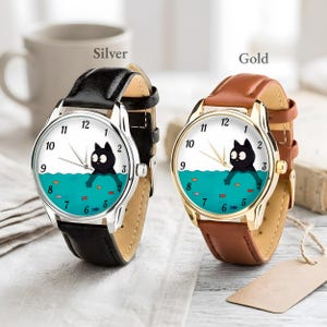 Pu&ograve; includere: Due orologi da polso, uno argentato e uno dorato, ciascuno con cinturino in pelle. I quadranti presentano un gatto dei cartoni animati nell'acqua con pesci. L'orologio argentato ha un cinturino nero, e quello dorato un cinturino marrone.