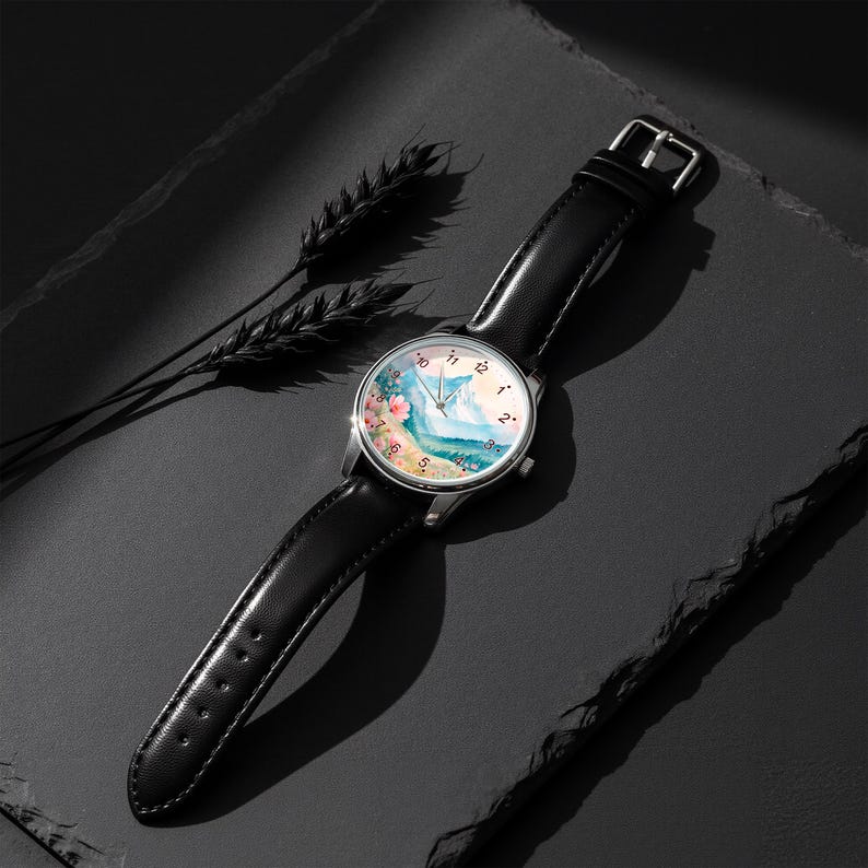 May include: A wristwatch with a black leather strap and a silver-tone circular case. The watch face features a colorful watercolor-style illustration of a mountain landscape with pink flowers, black numerals, and thin silver hands.