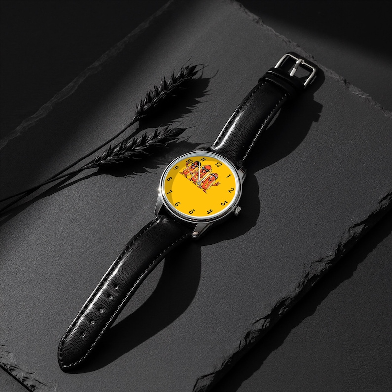 May include: A wristwatch with a black leather strap and a round silver-tone case. The watch face is bright yellow with black numerals and features a central graphic illustration of three anthropomorphic hot dogs wearing sunglasses.