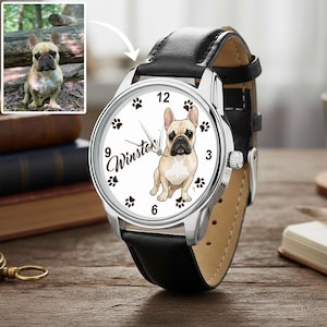 May include: A silver wristwatch with a black leather band. The watch face features a tan and white French Bulldog illustration, paw prints, and the name "Winston". A smaller image of the dog is in the upper left corner.
