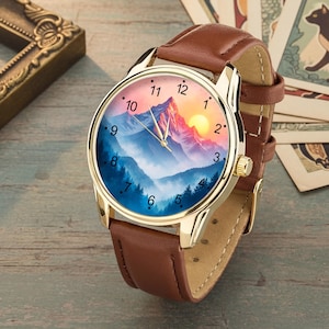 May include: A gold-toned wristwatch with a brown leather band. The watch face features a mountain landscape with a sunset. The watch has a gold bezel and a brown leather strap. The watch face has black numerals.