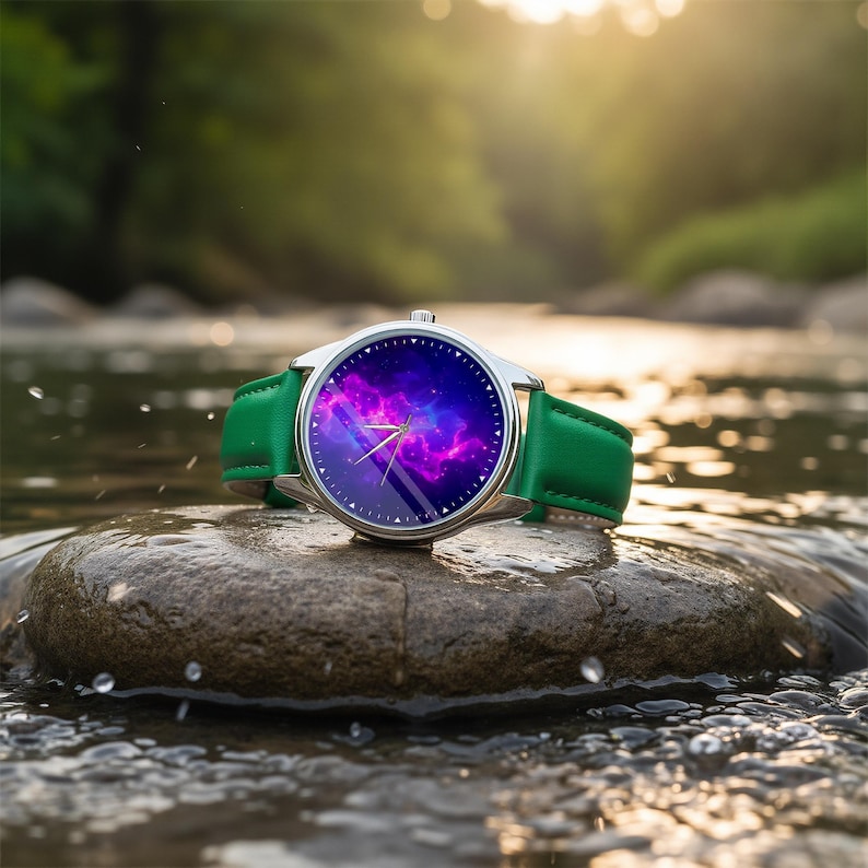 May include: A silver wristwatch with a green leather band rests on a rock in a stream. The watch face displays a vibrant purple and blue galaxy design. The watch hands show the time. The background is a blurred view of a green forest.