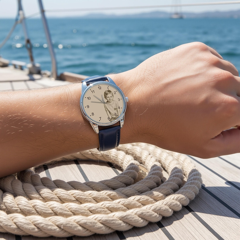 May include: A wristwatch with a silver case and a navy blue leather band. The watch face features a sepia-toned photograph of a child. The watch is being worn on a person's wrist.