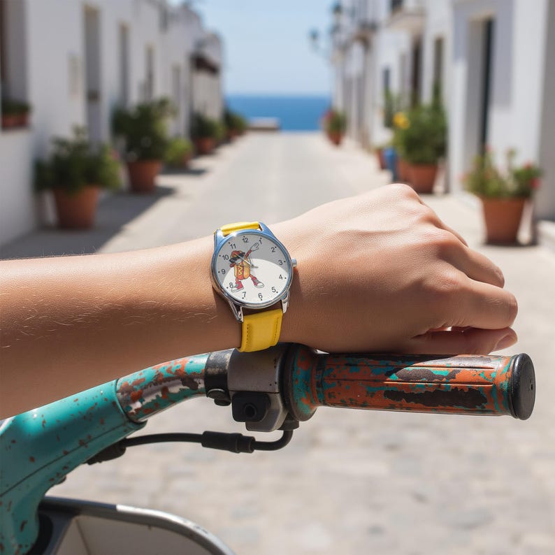 May include: A wristwatch with a bright yellow leather strap and a silver-tone metal case. The white watch face features black numerals and a central graphic illustration of a cartoon hot dog character wearing sunglasses and a red cap.