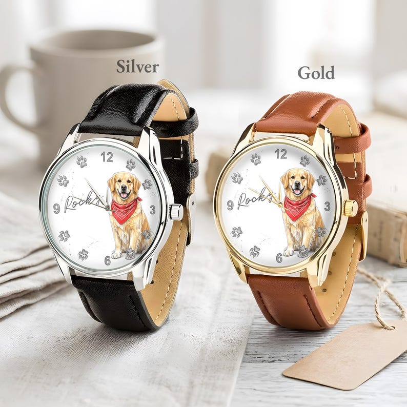Puede incluir: Dos relojes con correas de cuero. Uno tiene una caja plateada y una correa negra, el otro una caja dorada y una correa marr&oacute;n. Ambos relojes tienen una esfera blanca con una ilustraci&oacute;n de Golden Retriever con un pa&ntilde;uelo rojo. La palabra "Rocky's" est&aacute; escrita.