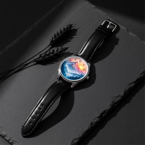 May include: A wristwatch with a black leather band and a silver-colored case. The watch face features a landscape design with mountains, trees, and a sunset. The watch is displayed on a dark surface.