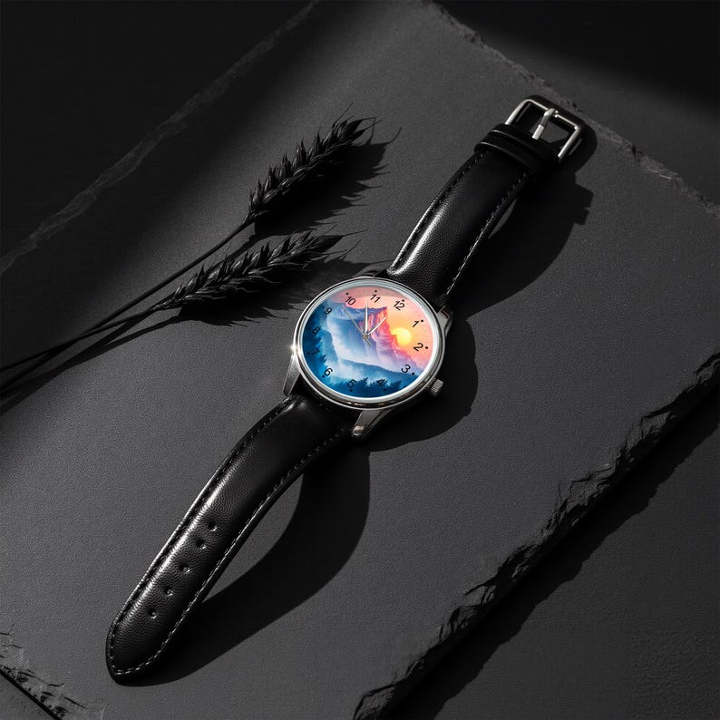 May include: A wristwatch with a black leather band and a silver-colored case. The watch face features a landscape design with mountains, trees, and a sunset. The watch is displayed on a dark surface.