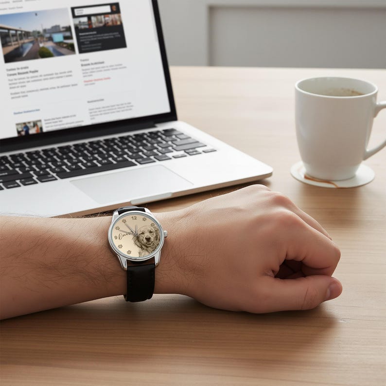 Pu&ograve; includere: Un orologio da polso con cinturino in pelle nera e cassa color argento. Il quadrante dell'orologio presenta un ritratto di un cane golden retriever. L'orologio &egrave; al polso di una persona, vicino a un laptop e una tazza di caff&egrave;.
