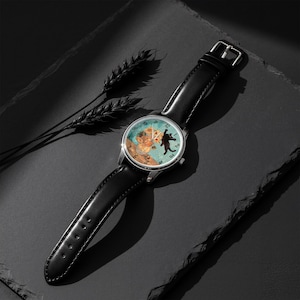 Puede incluir: Un reloj de pulsera con una correa de cuero negro y una caja plateada. La esfera del reloj presenta una ilustraci&oacute;n caprichosa de un oso y un gato. El fondo de la esfera es de color azul claro.