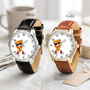 May include: Two analog wristwatches with white faces featuring a cartoon pizza slice dabbing while wearing sunglasses and red sneakers. One watch has a silver-tone case with a black leather strap, and the other has a gold-tone case with a brown leather strap.