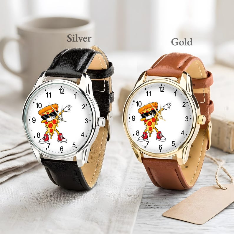 May include: Two analog wristwatches with white faces featuring a cartoon pizza slice dabbing while wearing sunglasses and red sneakers. One watch has a silver-tone case with a black leather strap, and the other has a gold-tone case with a brown leather strap.