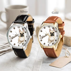 May include: Two wristwatches, one silver and one gold, each with a leather band. The watch faces feature a French bulldog illustration, paw prints, and the name "Winston". The silver watch has a black band, and the gold watch has a brown band.