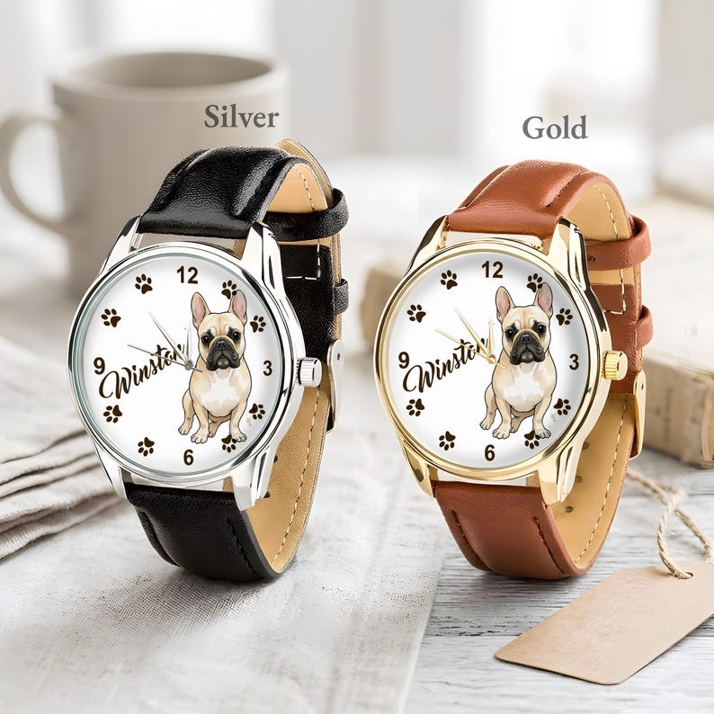 May include: Two wristwatches, one silver and one gold, each with a leather band. The watch faces feature a French bulldog illustration, paw prints, and the name "Winston". The silver watch has a black band, and the gold watch has a brown band.