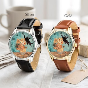 Puede incluir: Dos relojes de pulsera, uno plateado y otro dorado, cada uno con una correa de cuero. Las esferas de los relojes presentan una pintura de girasoles en un jarr&oacute;n y un gato negro. El reloj plateado tiene una correa negra, y el dorado una correa marr&oacute;n.