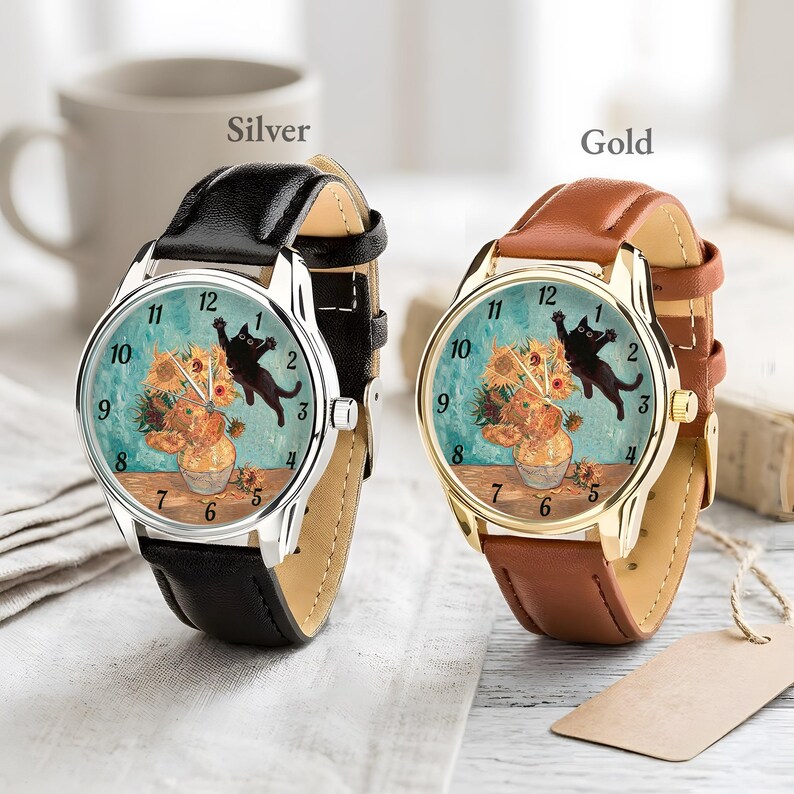 Puede incluir: Dos relojes de pulsera, uno plateado y otro dorado, cada uno con una correa de cuero. Las esferas de los relojes presentan una pintura de girasoles en un jarr&oacute;n y un gato negro. El reloj plateado tiene una correa negra, y el dorado una correa marr&oacute;n.