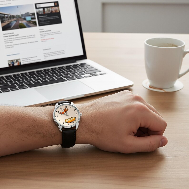 May include: A wristwatch with a silver-tone case and a black leather strap. The watch face is off-white and features a graphic illustration of a hot dog and a sausage, with black numerals and thin black hands to indicate the time.
