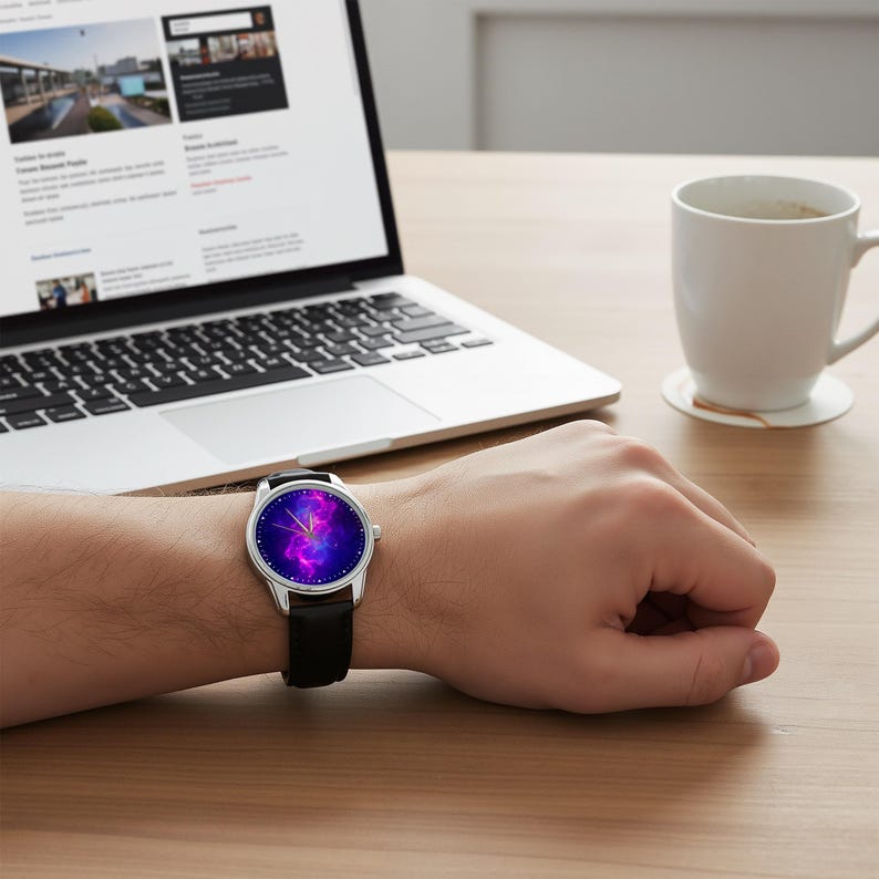 May include: A wristwatch with a black leather band and a silver case. The watch face displays a vibrant galaxy design in shades of purple, pink, and blue. The watch is on a person's wrist, with a laptop and coffee cup in the background.