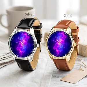 May include: Two watches with leather bands. One has a silver case and a black band, the other has a gold case and a brown band. Both watches have a blue and purple galaxy design on the watch face.