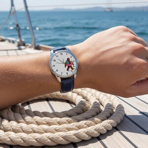May include: A wristwatch with a silver-tone case and a dark blue leather strap. The white watch face features black numerical hour markers and a central graphic of a brown creature wearing a blue shirt and holding a pink flamingo pool float.