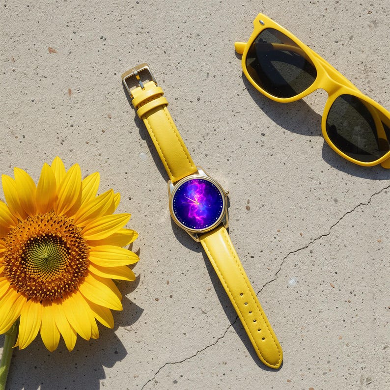 May include: A yellow watch with a gold case and a galaxy-themed face, paired with a matching yellow leather band. Beside the watch are yellow sunglasses and a bright yellow sunflower, all set against a concrete surface.