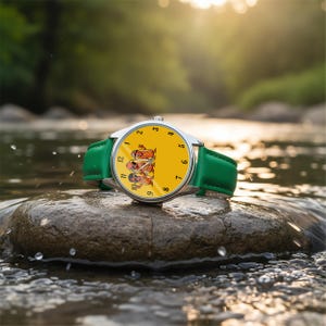 May include: A wristwatch with a bright yellow face featuring a cartoon illustration of three hot dogs wearing sunglasses. The watch has a silver-toned metal case and a smooth green leather strap with matching green stitching along the edges.