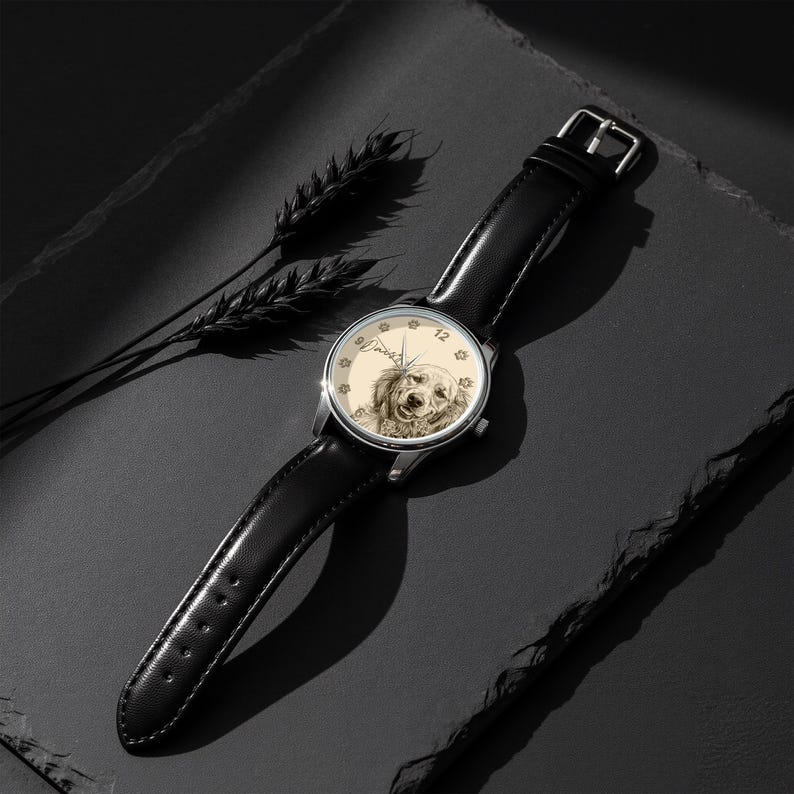 Pu&ograve; includere: Un orologio da polso con cinturino in pelle nera e cassa color argento. Il quadrante presenta un'illustrazione color seppia del volto di un cane, con impronte di zampe sul bordo. L'orologio &egrave; ambientato su uno sfondo scuro.