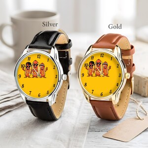 May include: Two wristwatches with yellow faces featuring a graphic of three cartoon hot dogs. One watch has a silver-tone case and a black leather strap, while the other has a gold-tone case and a brown leather strap. Both have black numerals.