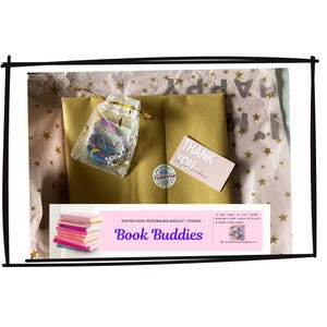 Può includere: Un pacco aperto con una busta di carta dorata, un piccolo biglietto rosa con la scritta "Grazie" e un sacchetto trasparente con un braccialetto colorato. Il pacco è avvolto in carta velina con stampa di stelle. Un banner in basso dice "Book Buddies".