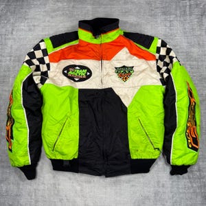 Könnte beinhalten: Eine neongrüne, schwarze und orangefarbene Racing-Jacke mit Reißverschluss und Karomuster an den Schultern und Ärmeln. Auf der Brust steht der Text Team Arctic Racing und Arctic Cat Racing. Die Ärmel haben orangefarbene Flammengrafiken.