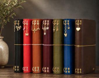 May include: Seven leather-bound journals in black, red, tan, maroon, olive green, blue, and dark brown. Each journal features gold-toned metal eyelets, a horizontal elastic closure, and various gold-toned charms including stars, hearts, and butterflies.