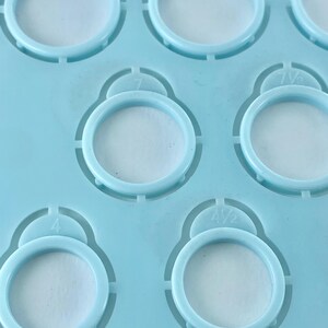 Pu&ograve; includere: Una dima in plastica azzurra per misurare gli anelli, dotata di molteplici fori circolari di varie dimensioni. Ogni foro &egrave; contrassegnato da un numero di misura specifico, inclusi 4, 4 1/2, 7 e 7 1/2, impresso direttamente sopra le aperture.
