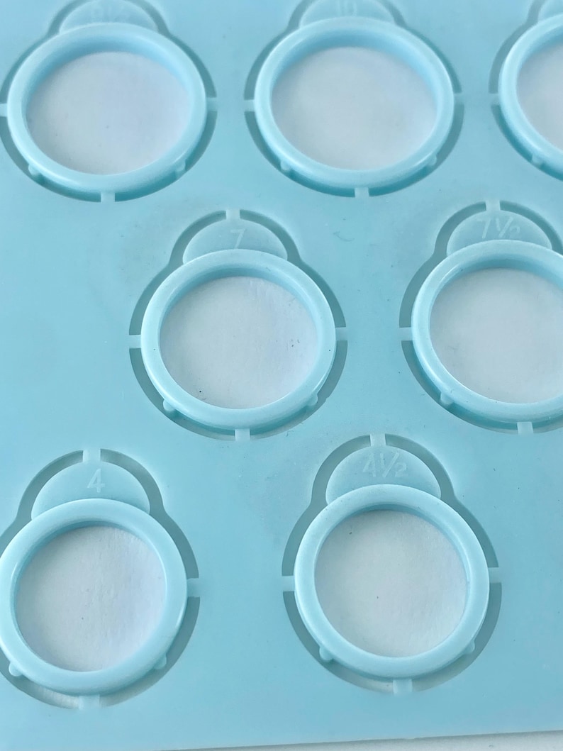 Pu&ograve; includere: Una dima in plastica azzurra per misurare gli anelli, dotata di molteplici fori circolari di varie dimensioni. Ogni foro &egrave; contrassegnato da un numero di misura specifico, inclusi 4, 4 1/2, 7 e 7 1/2, impresso direttamente sopra le aperture.