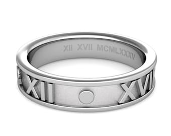 Può includere: Un anello in metallo color argento con numeri romani XII e XVII in rilievo sulla fascia esterna e un accento circolare. La fascia interna è incisa con il testo in numeri romani XII XVII MCMLXXXV in un carattere senza grazie.