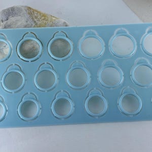 Pu&ograve; includere: Una dima rettangolare in plastica azzurra per misurare gli anelli, dotata di quindici fori circolari di diametri variabili. Lo strumento presenta una piccola linguetta sulla parte superiore di ogni cerchio e il testo www.myloveweddingring.com stampato verticalmente sul lato sinistro.