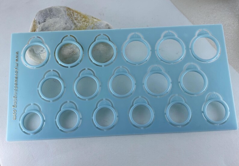 Pu&ograve; includere: Una dima rettangolare in plastica azzurra per misurare gli anelli, dotata di quindici fori circolari di diametri variabili. Lo strumento presenta una piccola linguetta sulla parte superiore di ogni cerchio e il testo www.myloveweddingring.com stampato verticalmente sul lato sinistro.