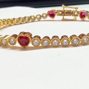 May include: Gold-toned bracelet featuring alternating round and heart-shaped gemstones. The bracelet has a clasp closure and is set with clear and red stones. The heart-shaped stones are a vibrant red color.