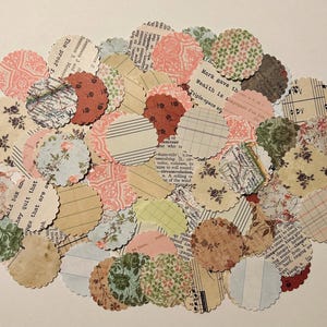 May include: A collection of scalloped-edge paper circles in various patterns and colors. The circles feature floral, striped, and patterned designs in shades of pink, green, beige, and brown. Some circles have text from old books.