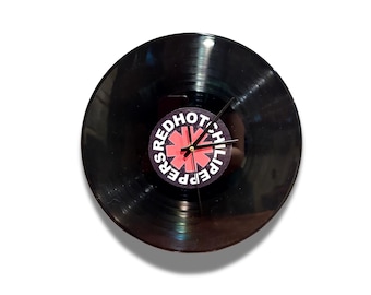 May include: A black vinyl record repurposed as a wall clock. The clock face features the Red Hot Chili Peppers logo in red and white. The clock hands are black and the clock is set against a white background.