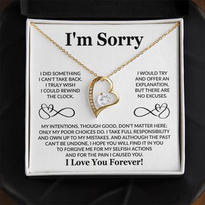 May include: A gold-colored heart-shaped pendant necklace with a clear gemstone center. The necklace is displayed in a white box with the words "I'm Sorry" and a heartfelt message printed on the inside.