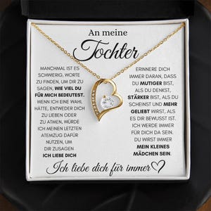 May include: A gold-colored heart-shaped pendant necklace with a clear gemstone at the center. The necklace is displayed in a white box with German text. The text includes the words "Tochter" and "Ich liebe dich für immer."