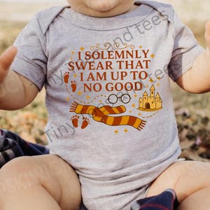 May include: A gray baby onesie with the text "I SOLEMNLY SWEAR THAT I AM UP TO NO GOOD" in brown and orange. The design includes a scarf, glasses, castle, and footprints.